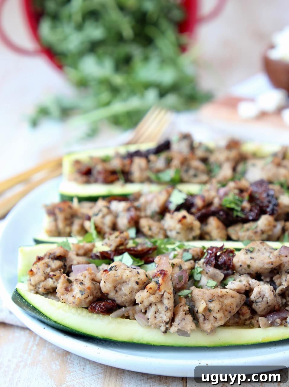 Greek Turkey Stuffed Zucchini Boats on white plate with gold forks in background, highlighting a healthy and vibrant meal.