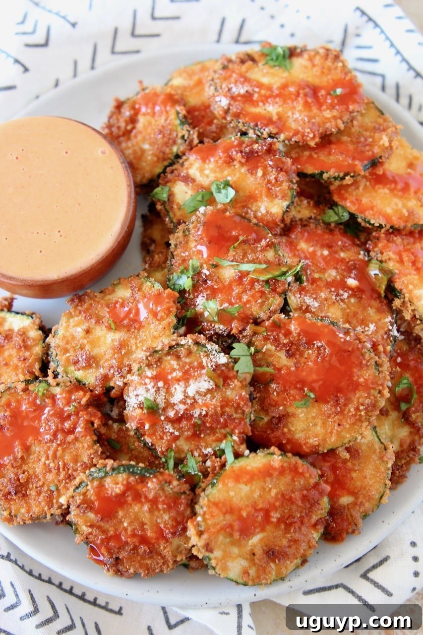 Crispy Zucchini Chips drizzled with buffalo sauce on plate with small bowl of buffalo blue cheese dressing