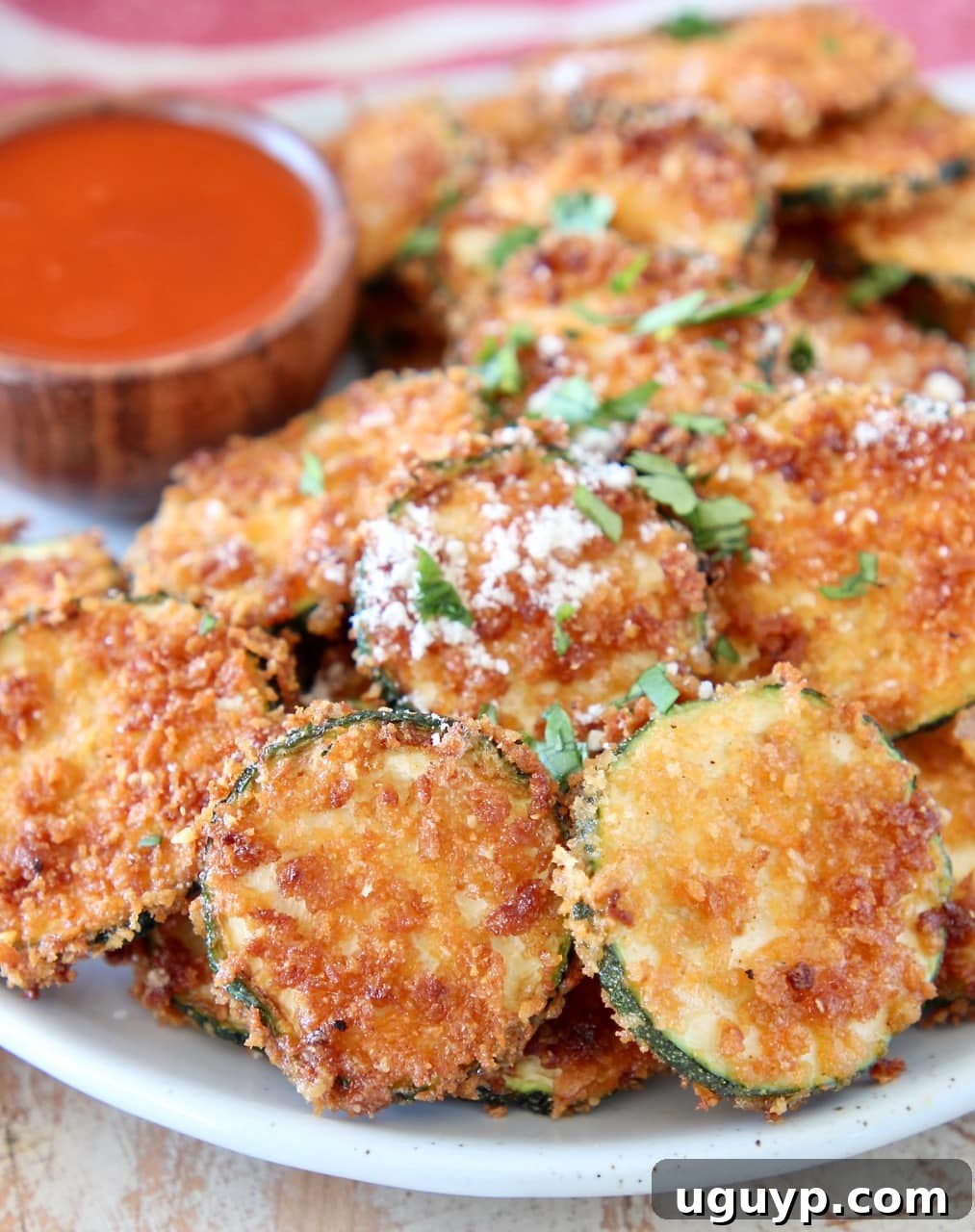 Crispy zucchini chips with parmesan cheese on plate with small bowl of buffalo sauce