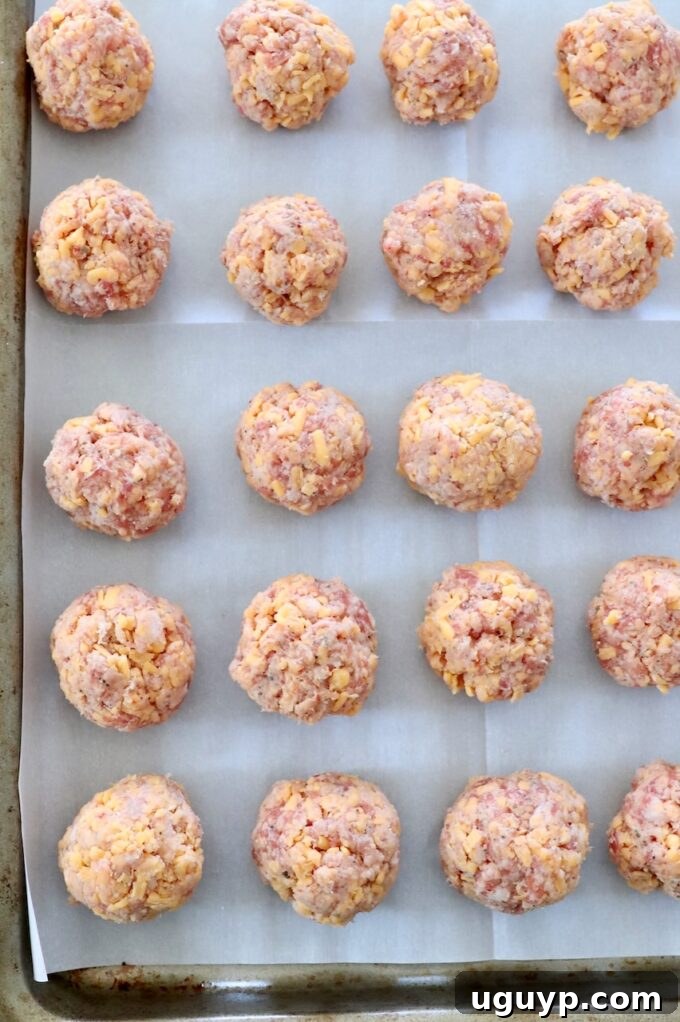 Uncooked Bisquick Sausage Balls neatly arranged on a parchment-lined baking sheet, ready for the oven.