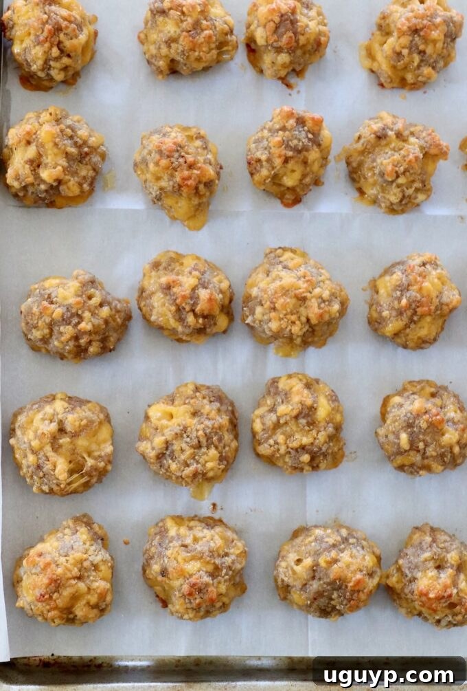 Freshly baked Bisquick Sausage Balls, golden brown and glistening, cooling slightly on a parchment-lined baking sheet.