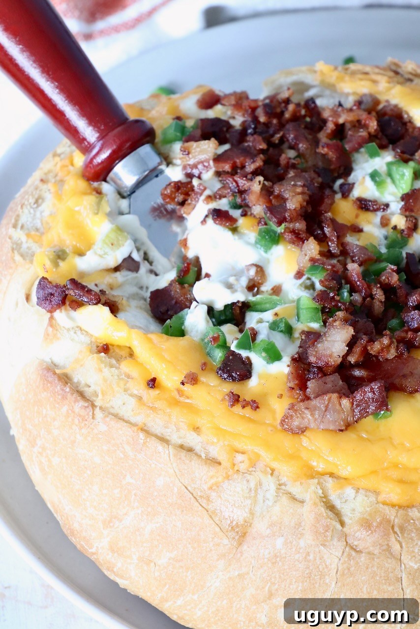 A round loaf of bread filled with melted cheese, crispy bacon bits, and vibrant diced jalapenos. A bread knife with a wooden handle is positioned on the side, inviting guests to dig in.