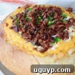 Round bread loaf hollowed and filled with melted cheese, topped with crispy bacon bits and chopped green peppers