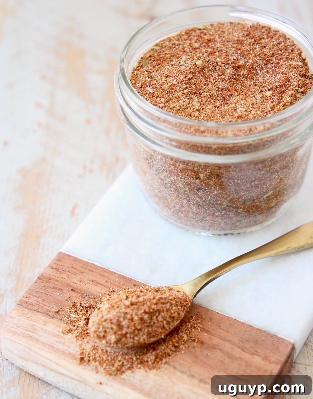 Homemade taco seasoning stored in a clear mason jar on a marble cutting board, with a spoon of seasoning beside it.