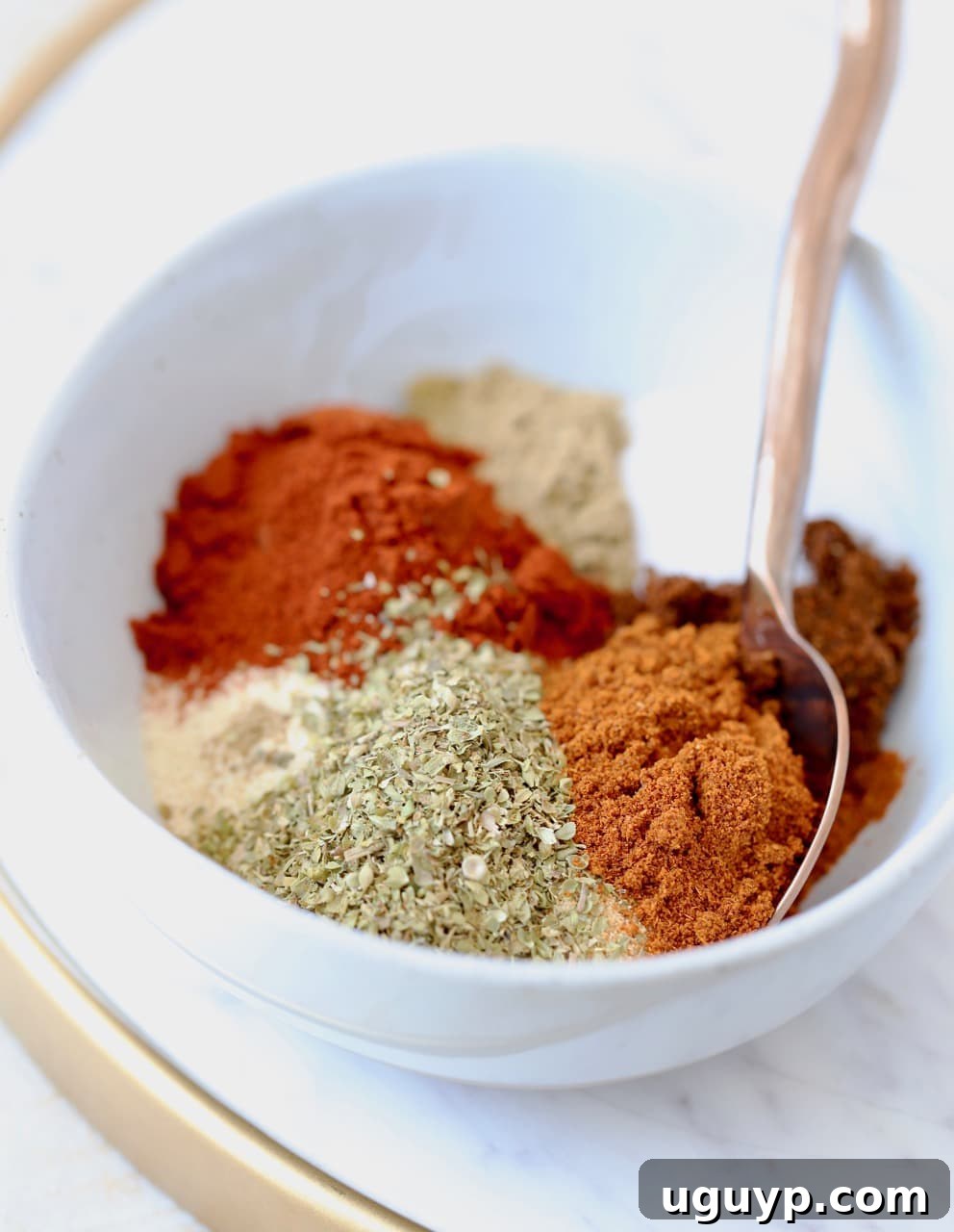 A bowl filled with homemade taco seasoning, showing the blend of 8 different spices, with a spoon for serving.