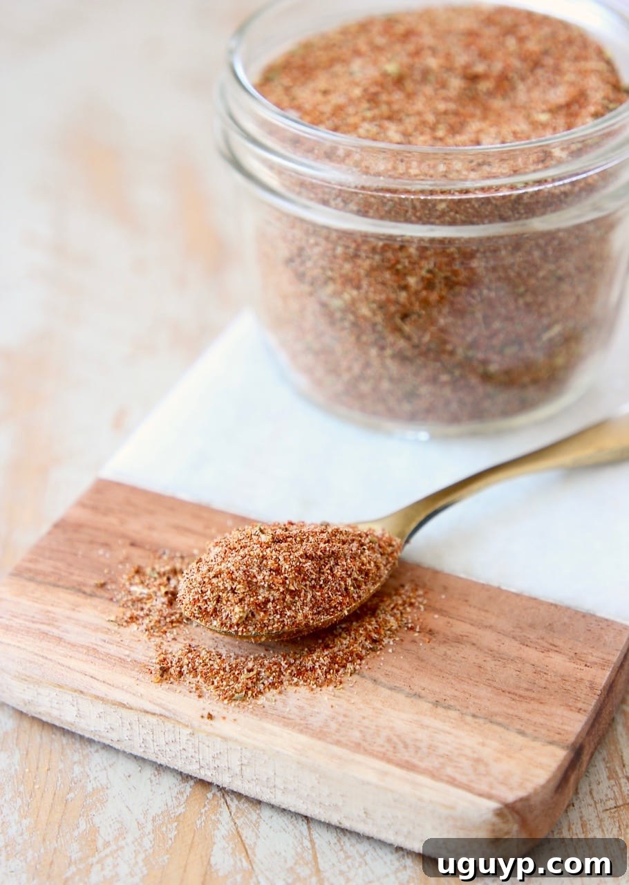 A mason jar filled with homemade taco seasoning sitting on a marble cutting board, with a small spoon displaying the seasoning.