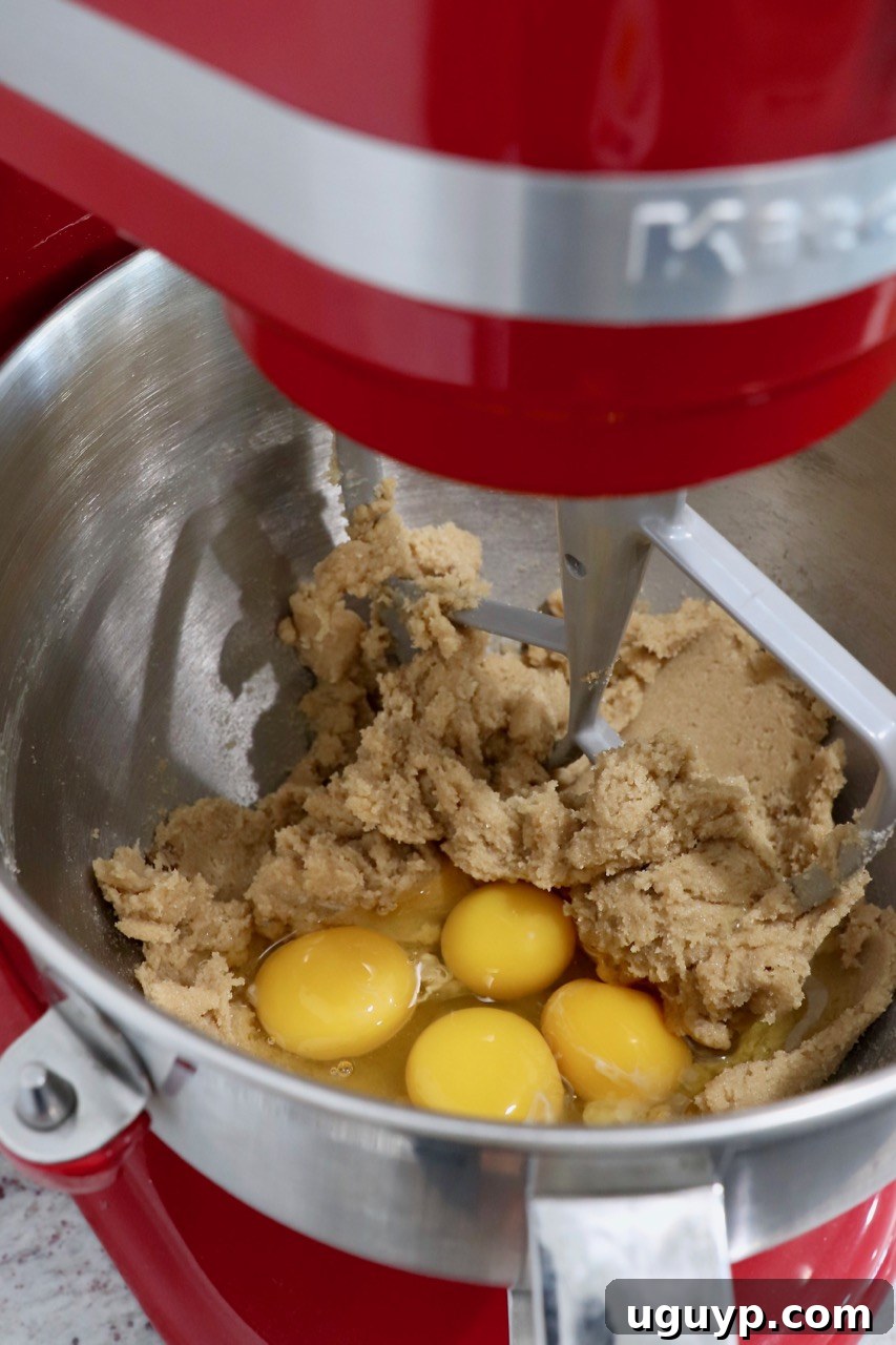 Cupcake batter in a stand mixer with raw eggs, ready to be mixed