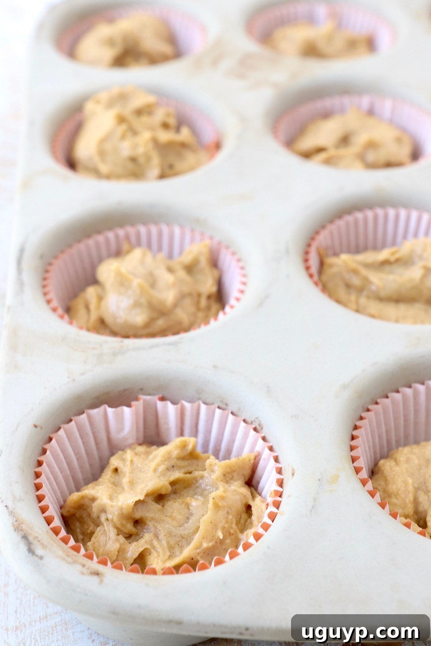 Cupcake liners in a muffin pan filled with pumpkin cupcake batter, ready for baking