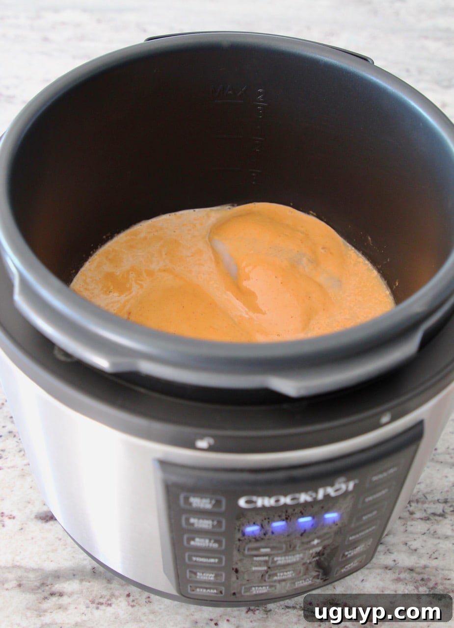 Chicken breasts and peanut sauce simmering in the Crock-Pot Express Crock Multi-Cooker, illustrating an in-progress step of the recipe.