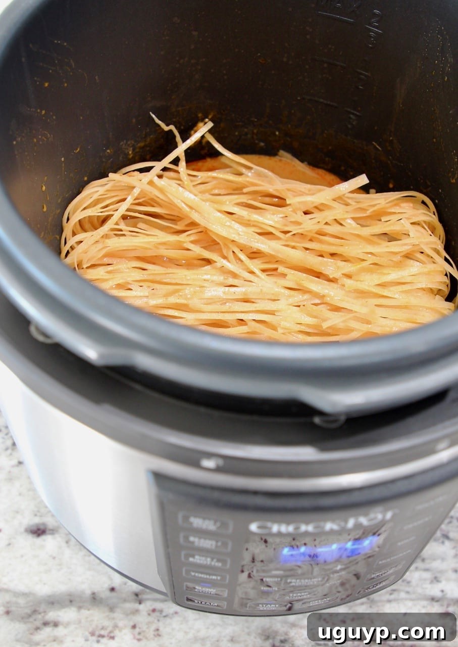 Rice noodles being added to the rich peanut sauce in the Crock-Pot Express Crock Multi-Cooker, demonstrating the effortless noodle cooking method.