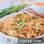 Pressure cooker chicken noodles with thai peanut sauce in bowl with diced green onions, shredded carrots and peanuts