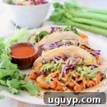 Buffalo cauliflower tacos on corn tortillas with jalapeno carrot slaw and fresh cilantro on plate with small bowl of buffalo sauce