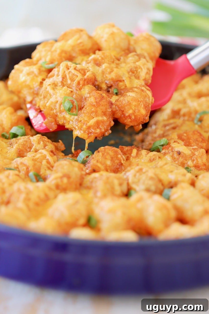Buffalo cheeseburger tater tot casserole in blue cast iron skillet with red spatula lifting casserole out of skillet
