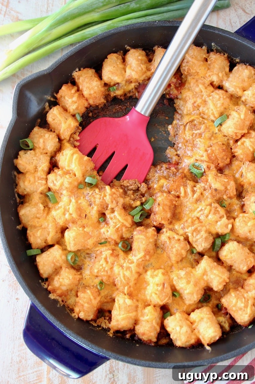Tater Tot Casserole in cast iron skillet with red spatula and green onions