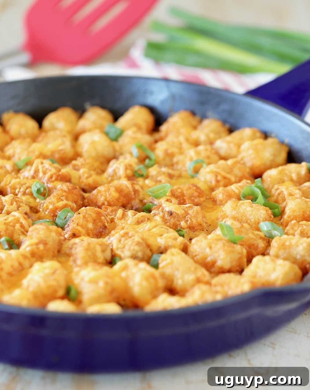 Tater Tot casserole with diced green onions in blue cast iron skillet with red spatula