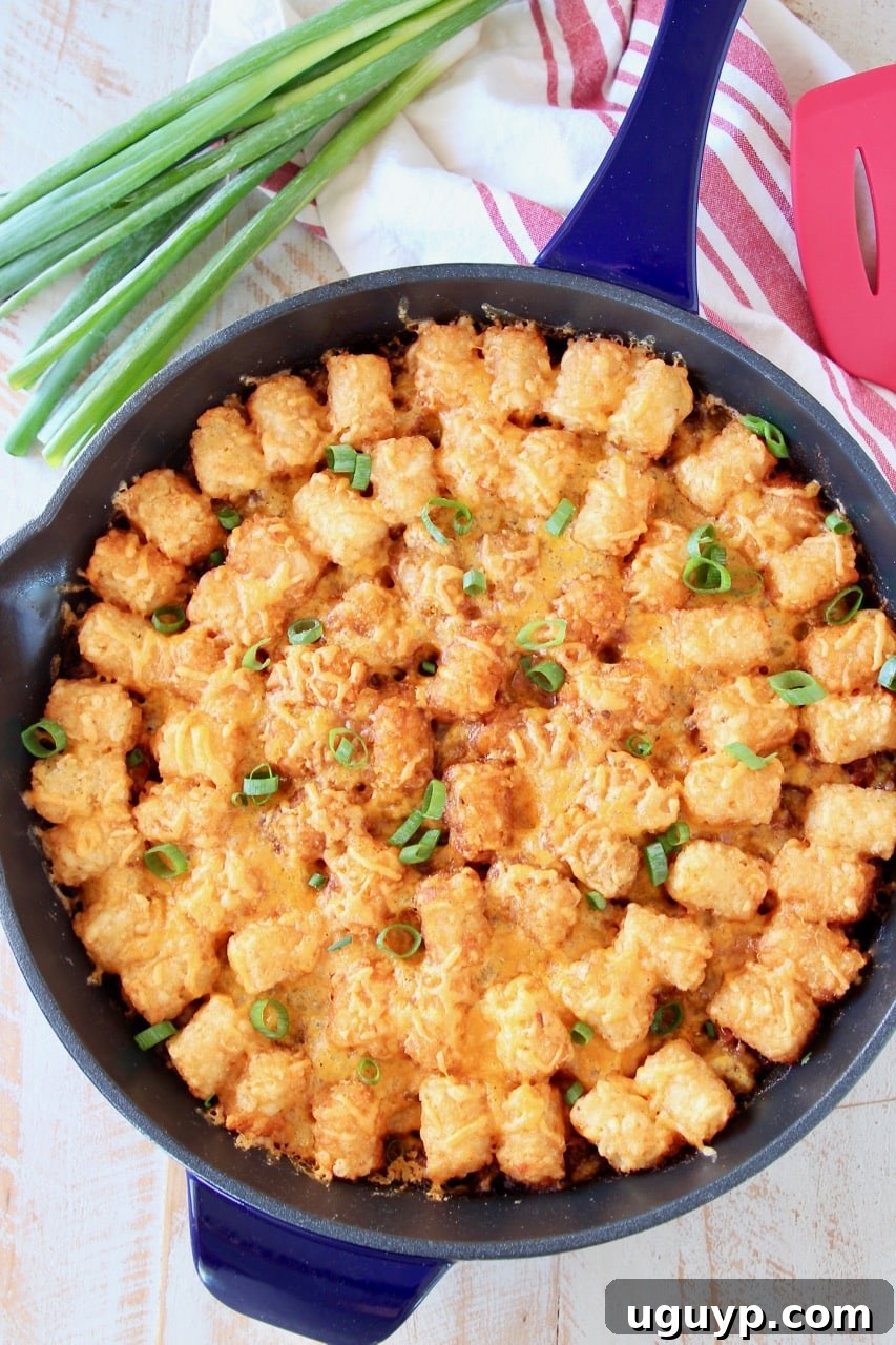 The best Tater Tot Casserole with ground beef and cheese in skillet with green onions and red striped towel