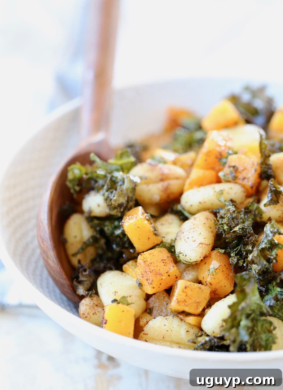 Golden-brown gnocchi, caramelized butternut squash, and crispy kale artfully arranged in a rustic bowl, ready to be served with wooden utensils.