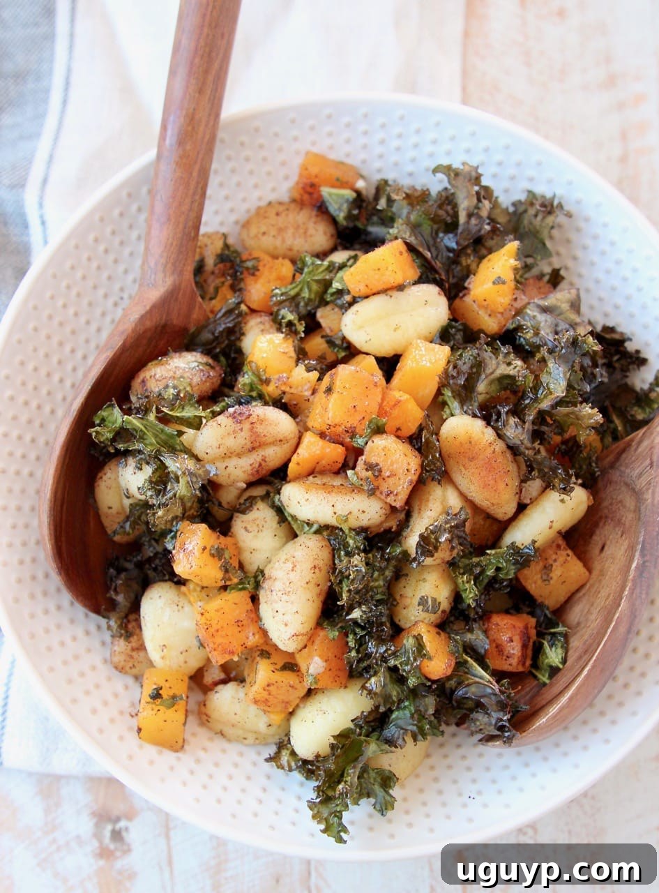 A generous serving of Sheet Pan Gnocchi with butternut squash and kale in a large white serving bowl, accompanied by wooden serving spoons.