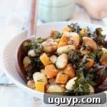 Baked gnocchi, butternut squash and kale in bowl with wooden serving spoons, whole butternut squash and green baking dish in back