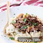 French onion pot roast on top of mashed potatoes on white plate with gold fork