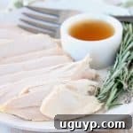 Sliced turkey breast on white plate with maple apple reduction in small white ramekin, large fork on side of plate and fresh rosemary sprigs