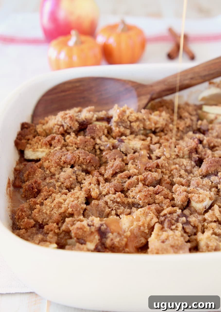 Pumpkin spice apple crumble in a rustic casserole dish, adorned with a wooden spoon and a rich drizzle of caramel syrup. Subtle ceramic pumpkins complete the cozy fall backdrop.