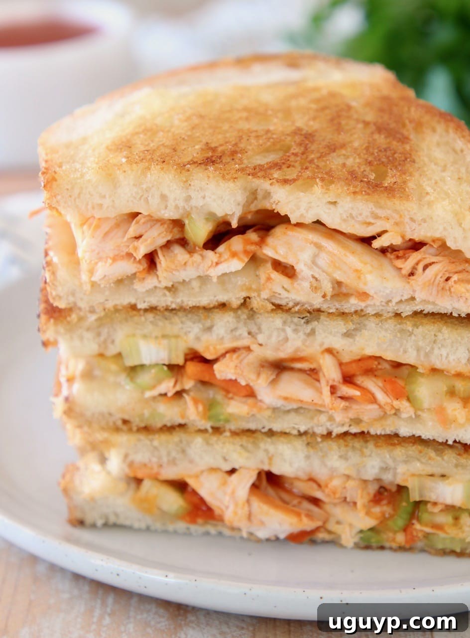 Buffalo turkey grilled cheese sandwiches, sliced in half diagonally, stacked up on white plate with fresh parsley in the background