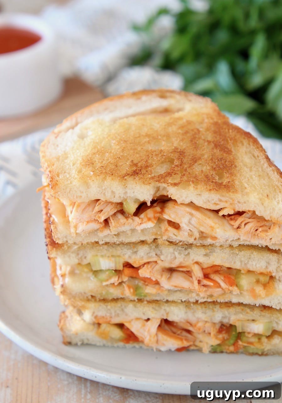 Buffalo turkey grilled cheese sandwiches, sliced in half diagonally, stacked up on white plate with fresh parsley in the background