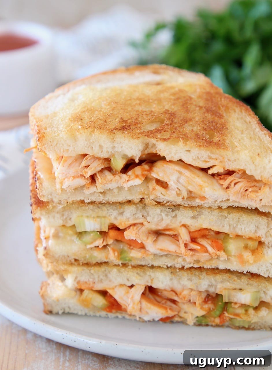 Buffalo turkey grilled cheese sandwiches, sliced in half diagonally, stacked up on white plate with fresh parsley in the background