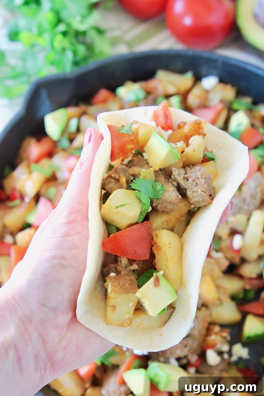 A hand holding a perfectly assembled breakfast taco in a soft flour tortilla, generously filled with savory diced potatoes, creamy avocado, crisp bell pepper, juicy tomatoes, and flavorful turkey sausage. This visually appealing taco highlights the versatility of the breakfast hash.