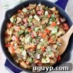 A hearty breakfast hash in a cast iron skillet, featuring a mix of potatoes, sausage, and vegetables, with a wooden spoon nestled in the pan. The skillet rests on a green and white striped towel, adding a rustic charm to the presentation.