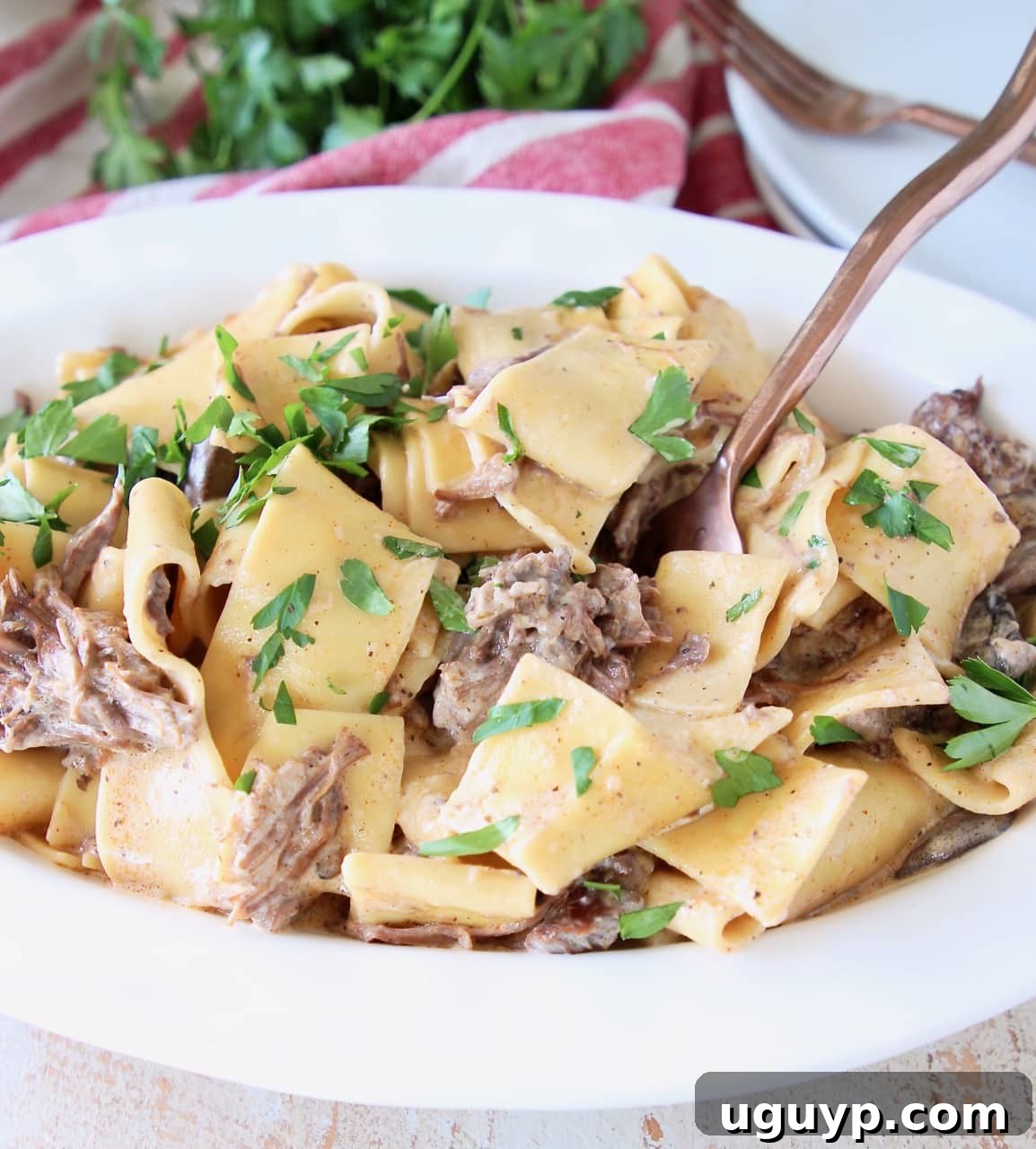 Instant pot beef stroganoff with wide egg noodles and fresh parsley in white serving bowl, with copper fork in bowl
