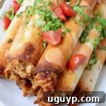 buffalo chicken taquitos stacked up on a plate topped with shredded lettuce and diced tomatoes