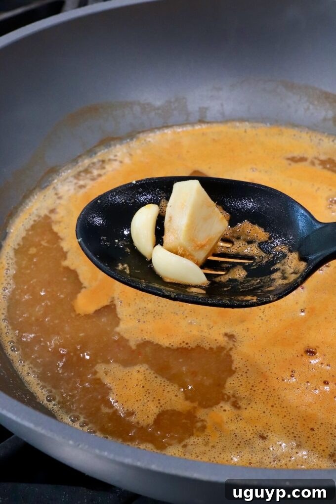 garlic cloves and ginger in a slotted spoon held above a pot of broth