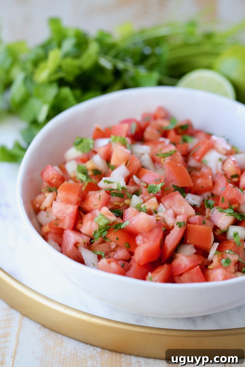 Fresh Pico de Gallo in a white bowl, garnished with cilantro and lime, on a marble tray.