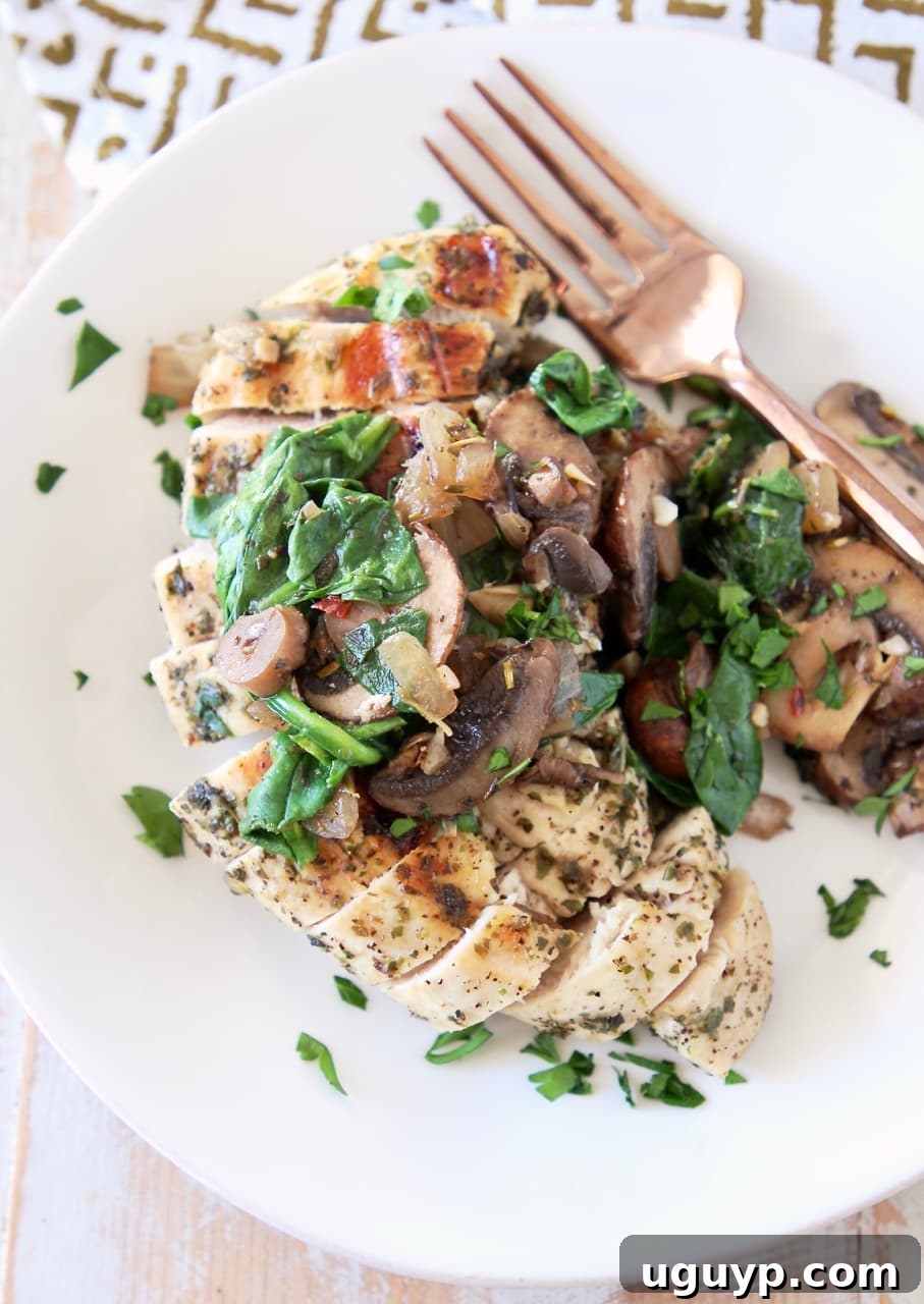 Sliced grilled chicken breast on a white plate, elegantly topped with sautéed mushrooms and fresh spinach, with a copper fork resting on the side.