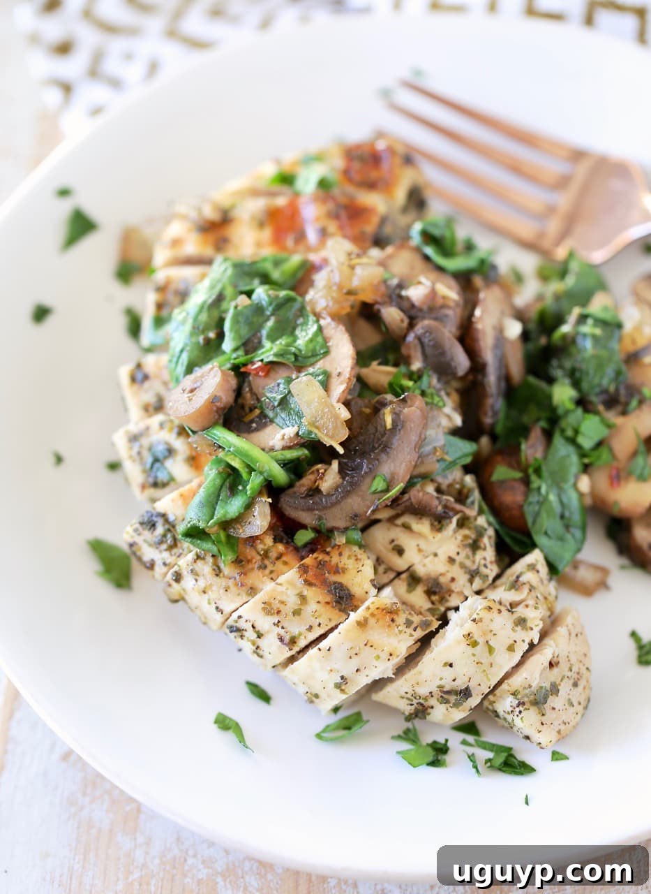 Grilled sliced chicken on a white plate, generously topped with sautéed mushrooms and spinach, with a copper fork at the side and garnished with fresh chopped parsley.