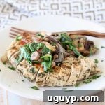 Sliced mushroom spinach chicken breast on a plate with a copper fork, resting on a gold and white patterned napkin.