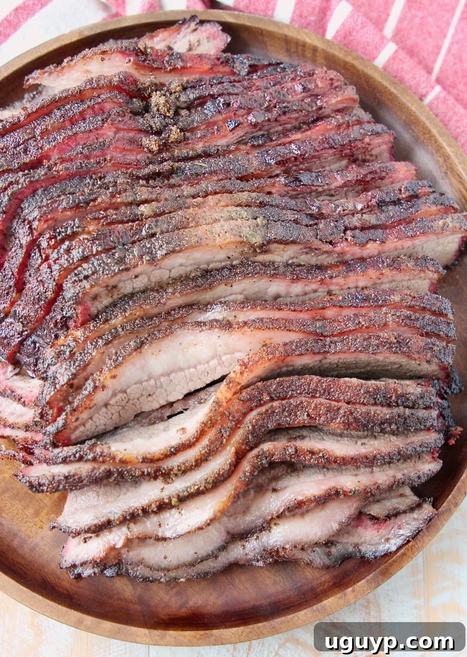 An overhead shot of a round wooden serving tray piled high with perfectly sliced, succulent smoked brisket.