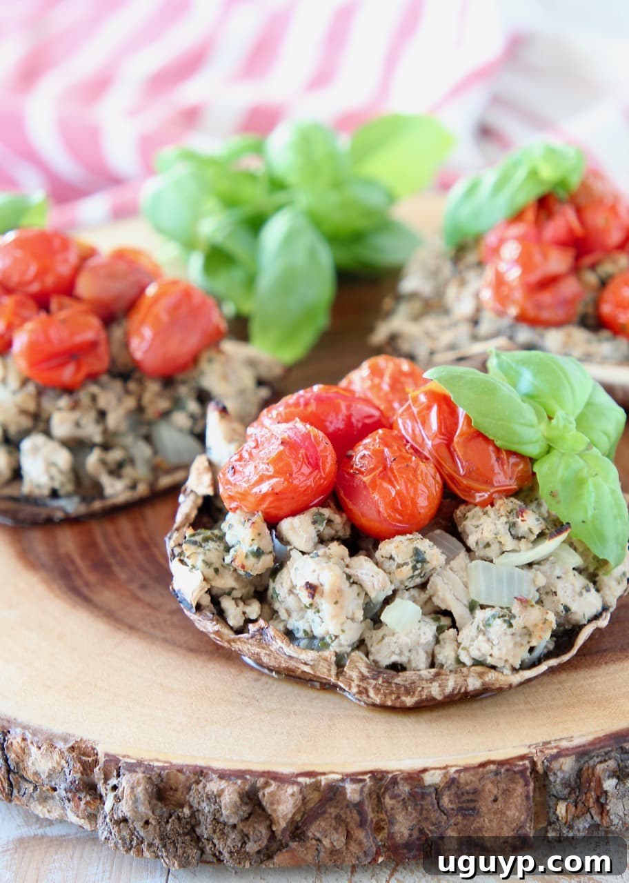 Delicious Baked Italian Stuffed Portobello Mushrooms, generously filled with seasoned ground turkey and vibrant cherry tomatoes, garnished with fresh basil, artfully arranged on a rustic wooden cutting board, with a charming red and white striped towel in the background.