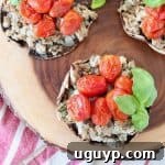 Overhead shot of stuffed portobello mushrooms filled with ground turkey, red cherry tomatoes and fresh basil leaves, sitting on a wood cutting board on top of a red and white striped towel