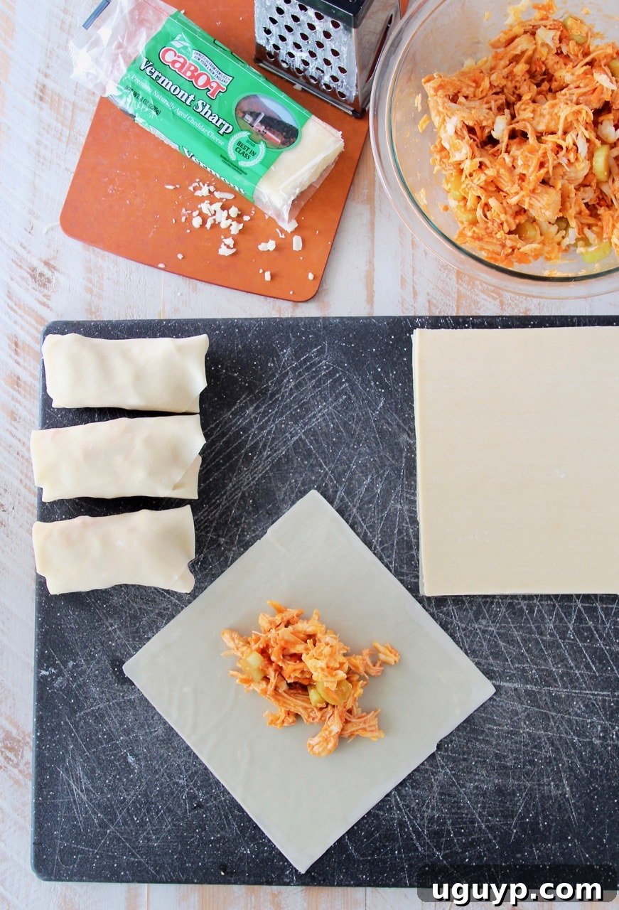 Detailed shot of the Buffalo Chicken Egg Roll preparation process, showing a hand carefully folding an egg roll wrapper filled with the chicken and cheese mixture, ready for pan-frying.