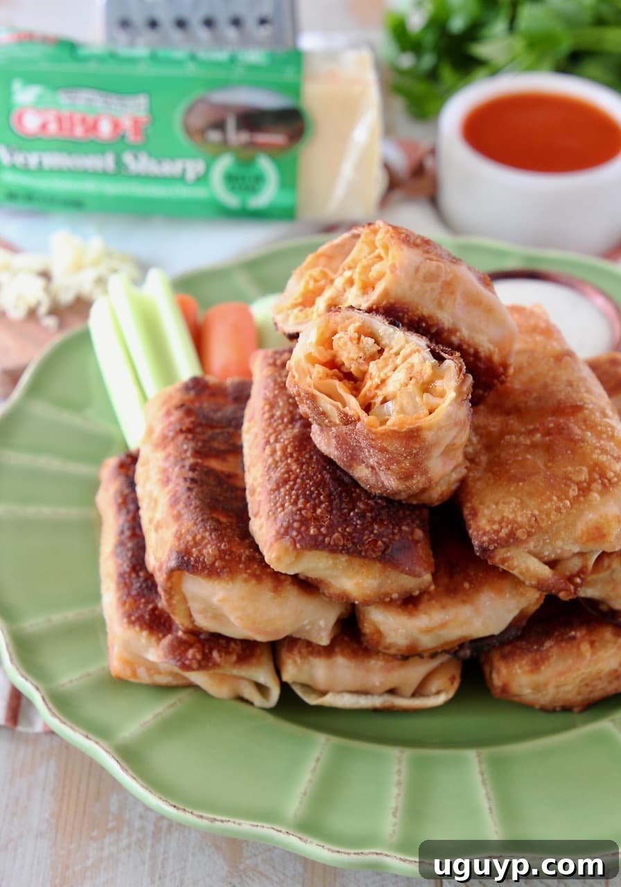 A close-up of golden-brown Buffalo chicken egg rolls stacked on a green plate, with the top egg roll halved to reveal its delicious, cheesy, and spicy filling.