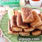 Buffalo chicken egg rolls piled up on a green plate with celery and carrots on the plate and a small wooden bowl filled with ranch dressing