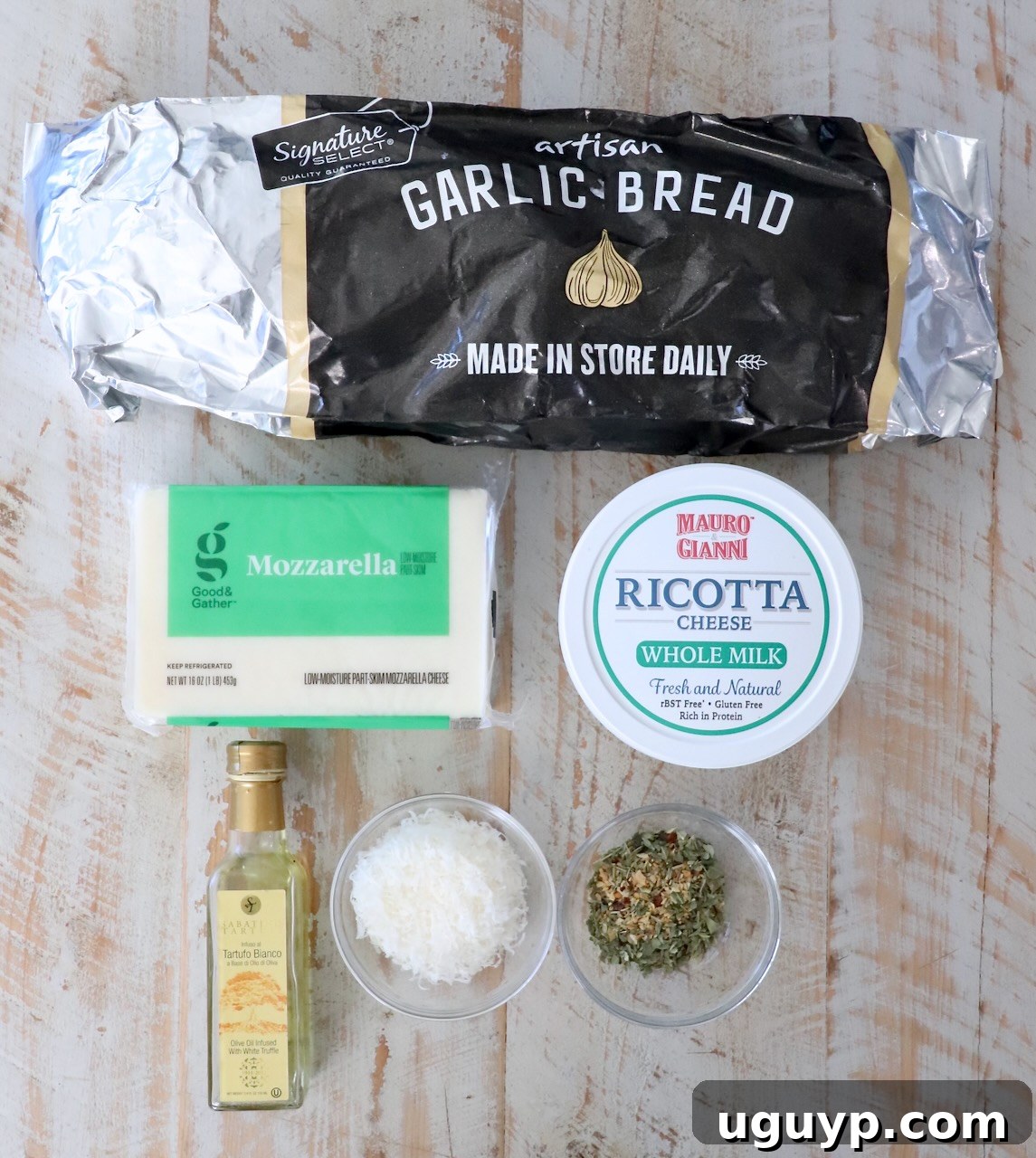 Packaged garlic bread on a wooden surface, surrounded by mozzarella, ricotta, olive oil, grated cheese, and herbs