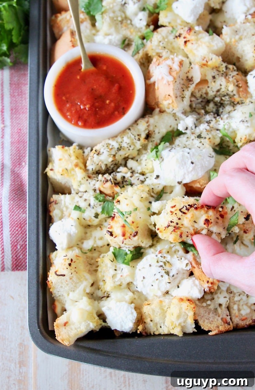 Hand grabbing a piece of garlic bread nachos off of a baking sheet with a small bowl of marinara sauce in the corner