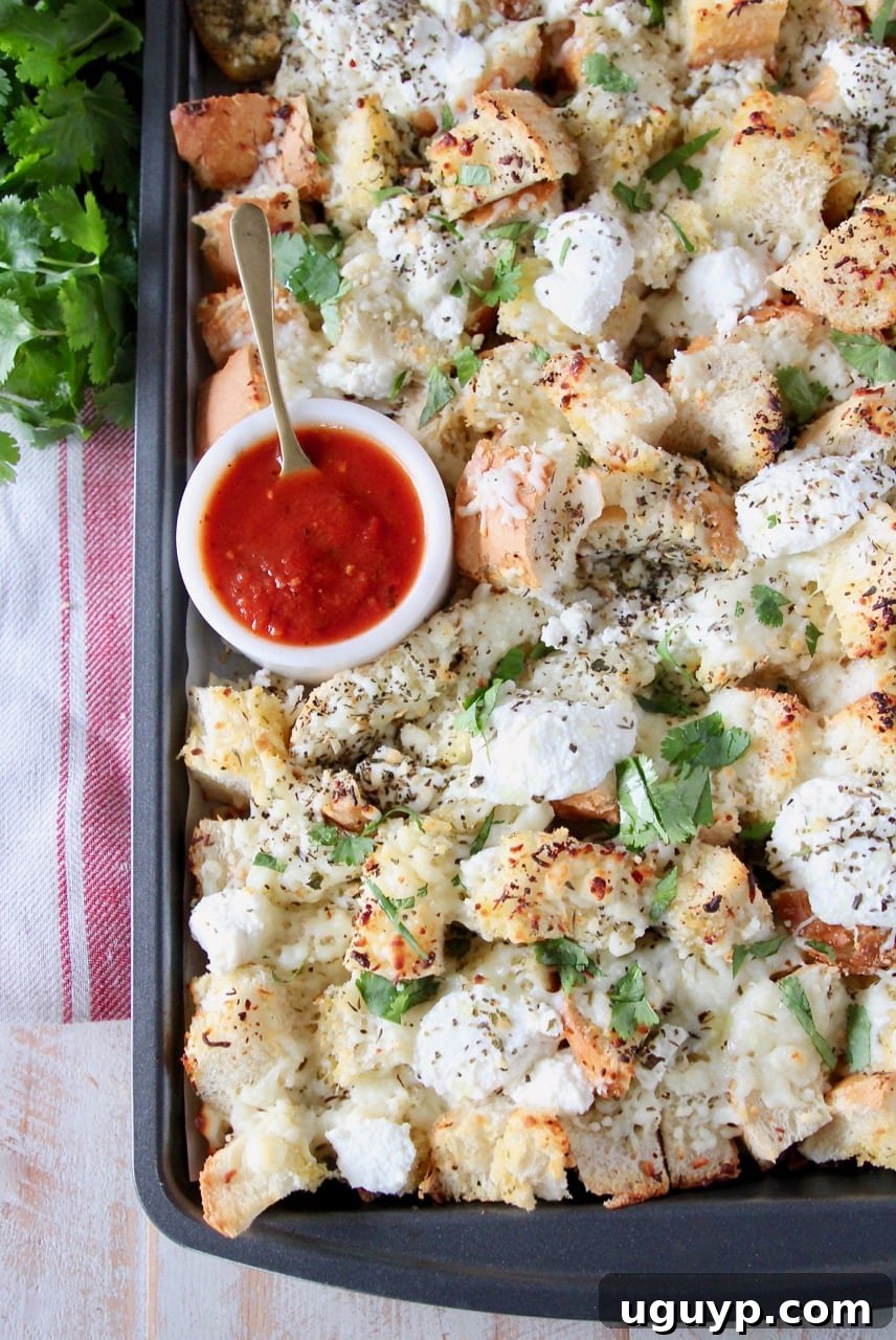 Cheesy garlic bread nachos on a baking sheet with a small bowl of marinara sauce in the corner with a spoon in the bowl