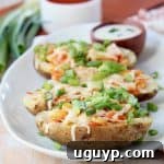 Buffalo chicken potato skins on white plate with green onions and bowl of buffalo sauce and bowl of ranch dressing in the background