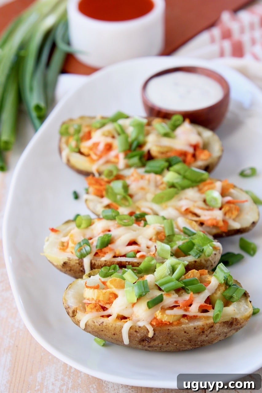 Buffalo chicken on potato skins, topped with diced green onions with a wood bowl of ranch dressing on the plate behind the potato skins