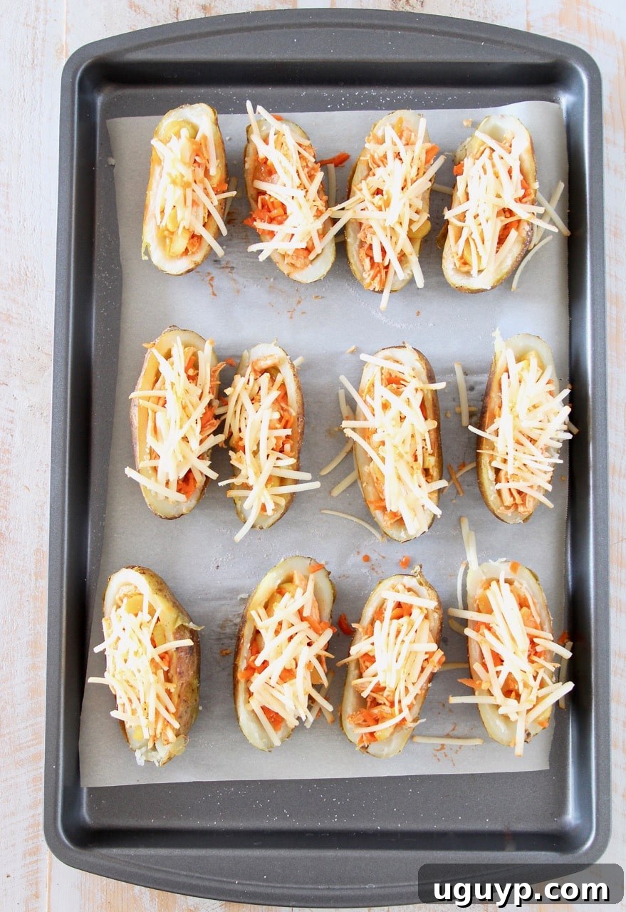 Potato skins filled with buffalo chicken and shredded cheddar cheese on baking sheet